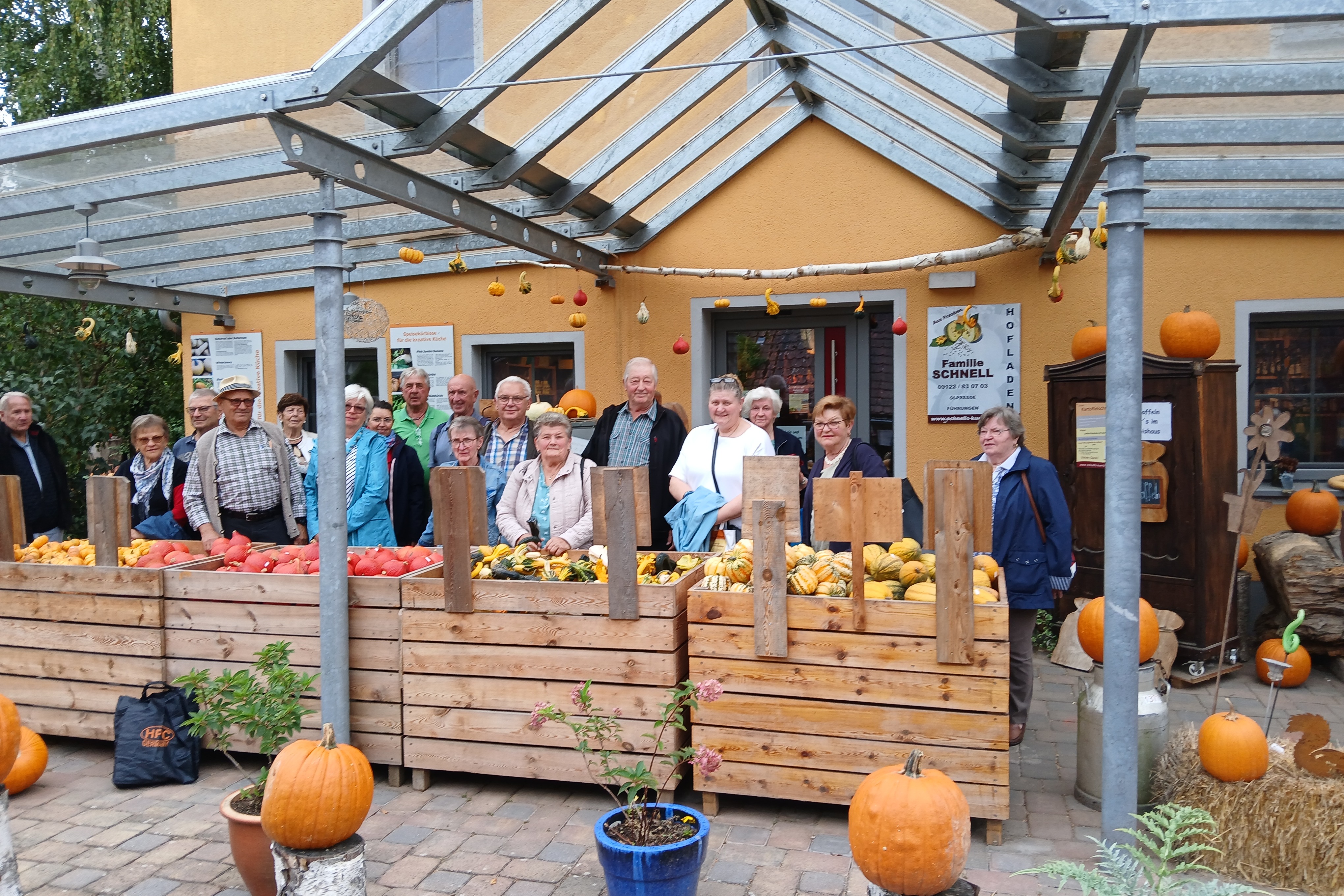 Kürbishof der Familie Schnell Gäste vor dem Hofladen, vor Paletten von verschiedenen farbigen Kürbissen (gelb, organge