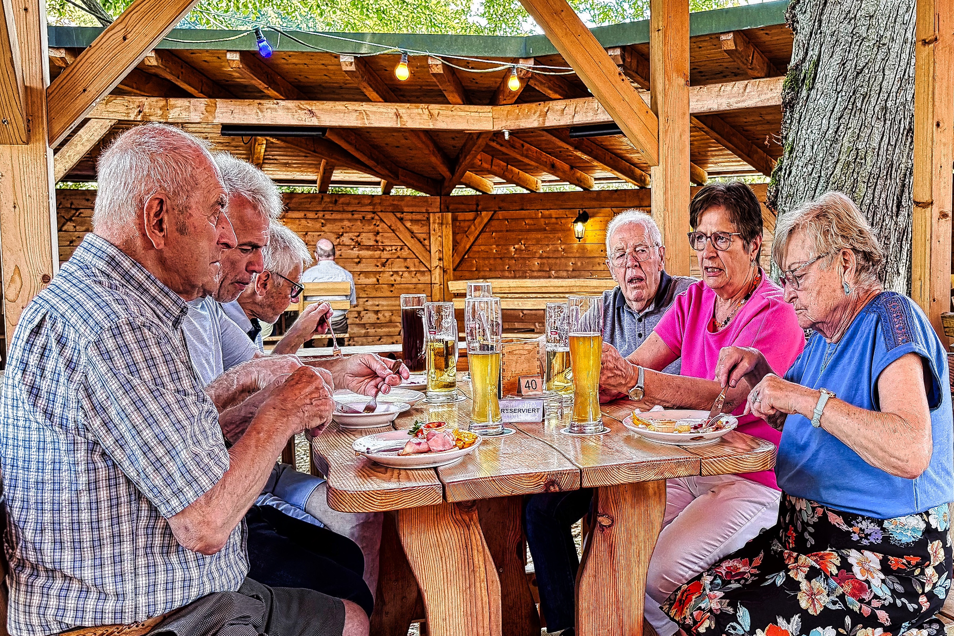 6 VdK-Mitglieder sitzen am Biertisch im Biergarten und unterhalten sich.