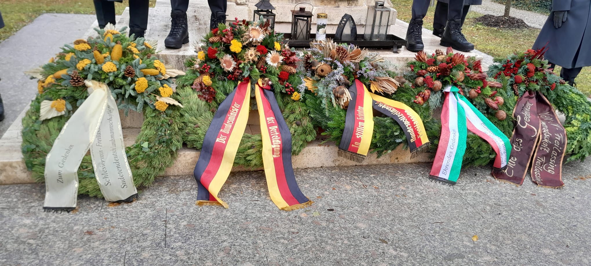 Kränze Verschiedene Kränze mit Schleifen liegen auf Sockel aus Beton