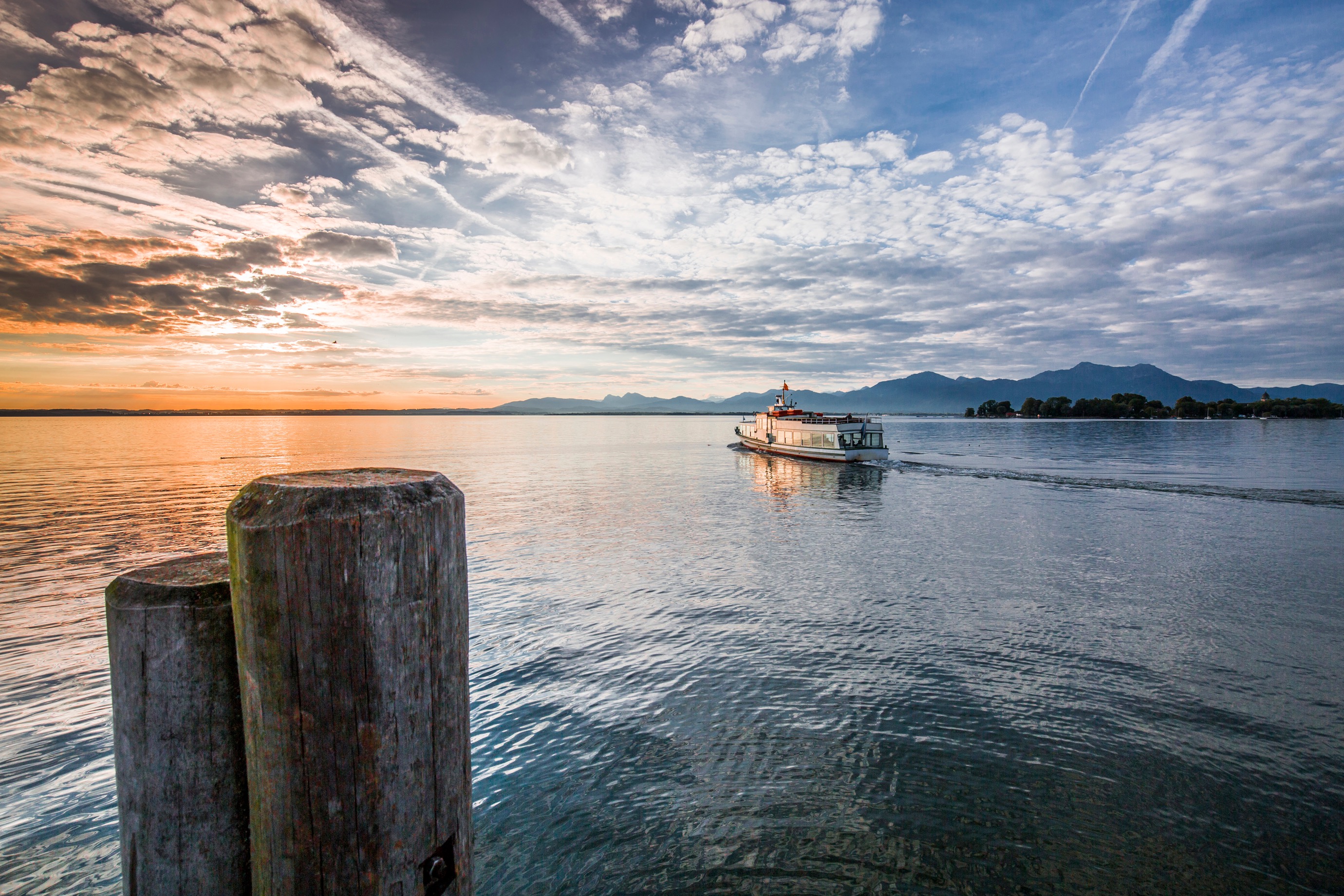 Auf dem Chiemsee bei Sonnenuntergang f&auml;hrt ein Schiff dem Horizont entgegen.