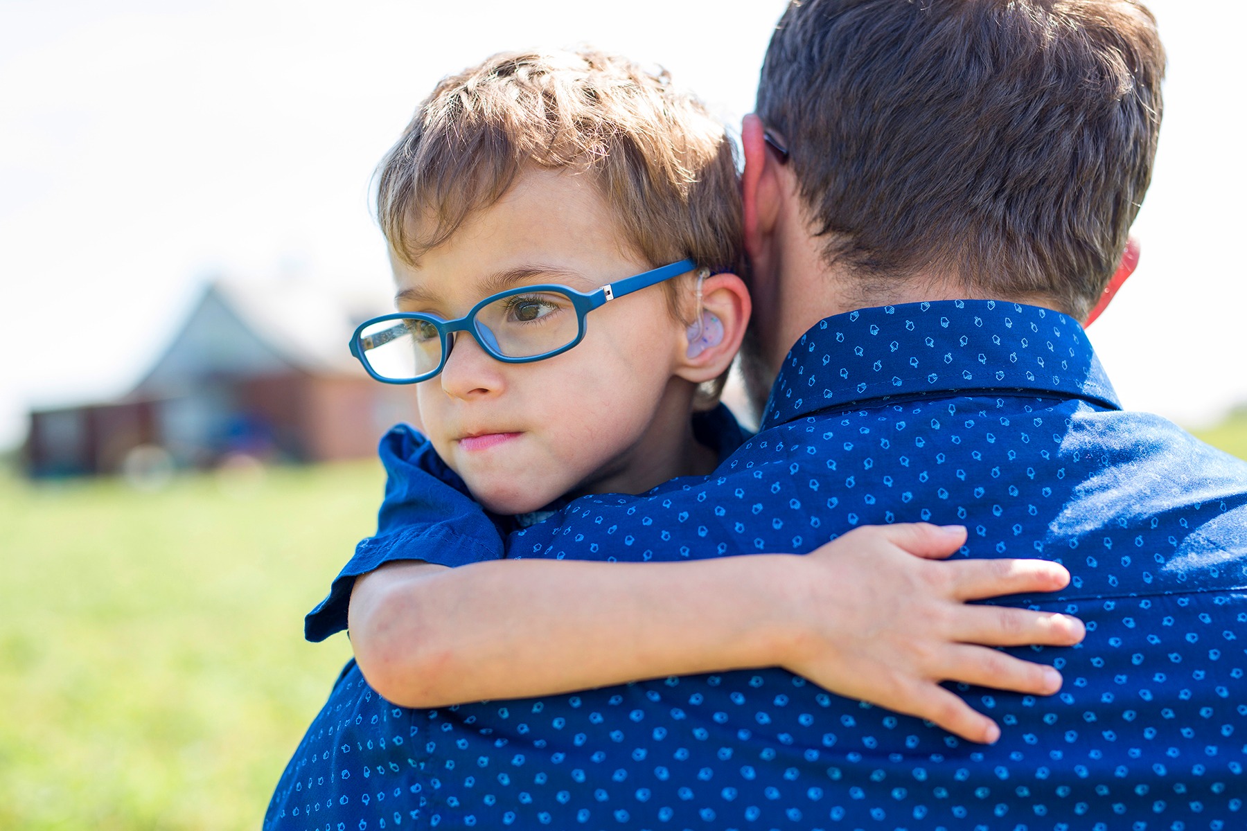 Ein kleiner Junge mit blauer Brille und H&ouml;rger&auml;ten auf dem Arm seines Vaters
