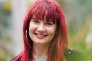 Zu sehen ist ein Portrait von Frau Dr. Sarah Straub, l&auml;chelnd und mit r&ouml;tlich gef&auml;rbten nackenlangen Haaren.