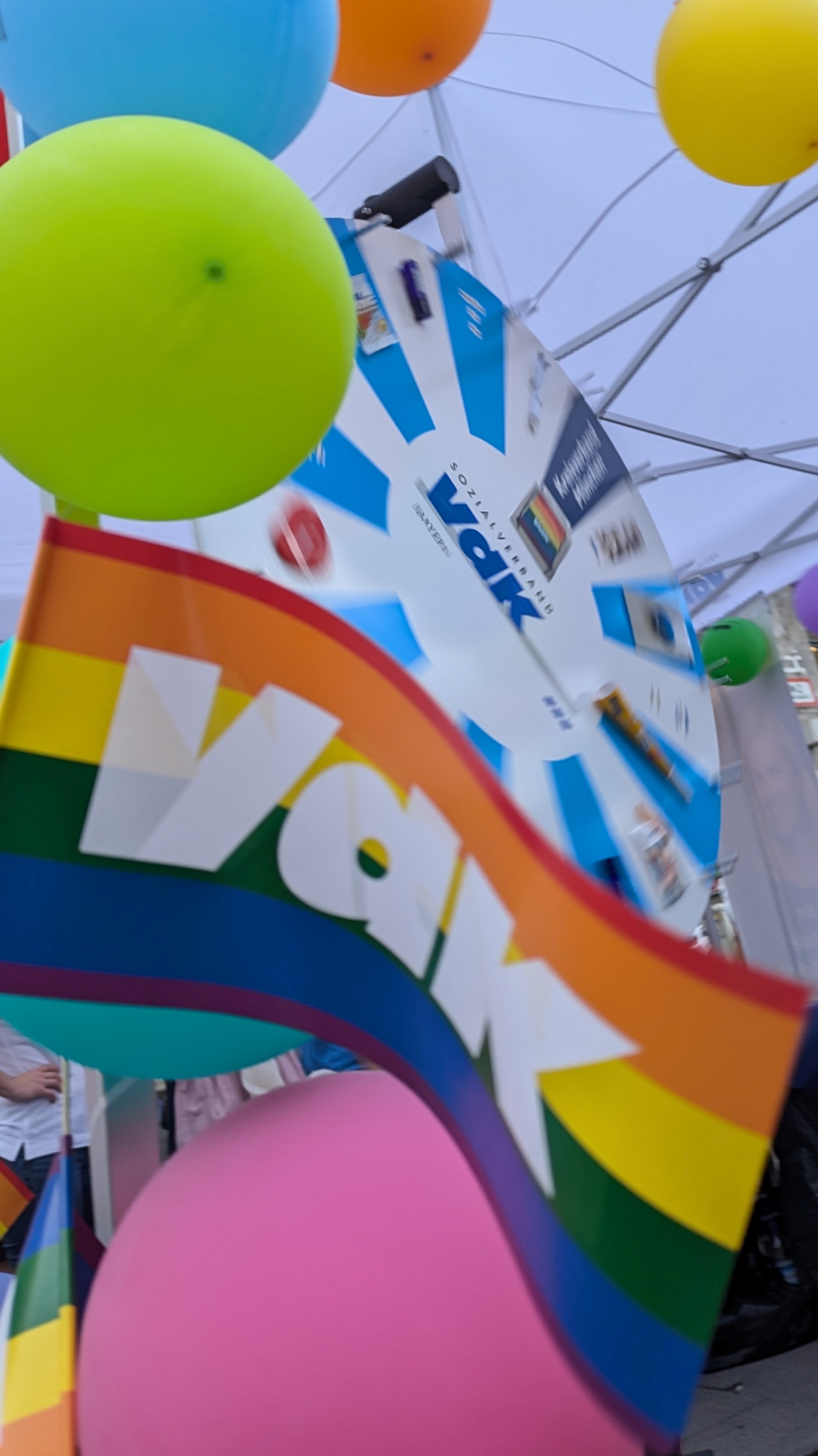 VdK Logo auf Regenbogenfarben-Flagge mit Glücksrad im Hintergrund