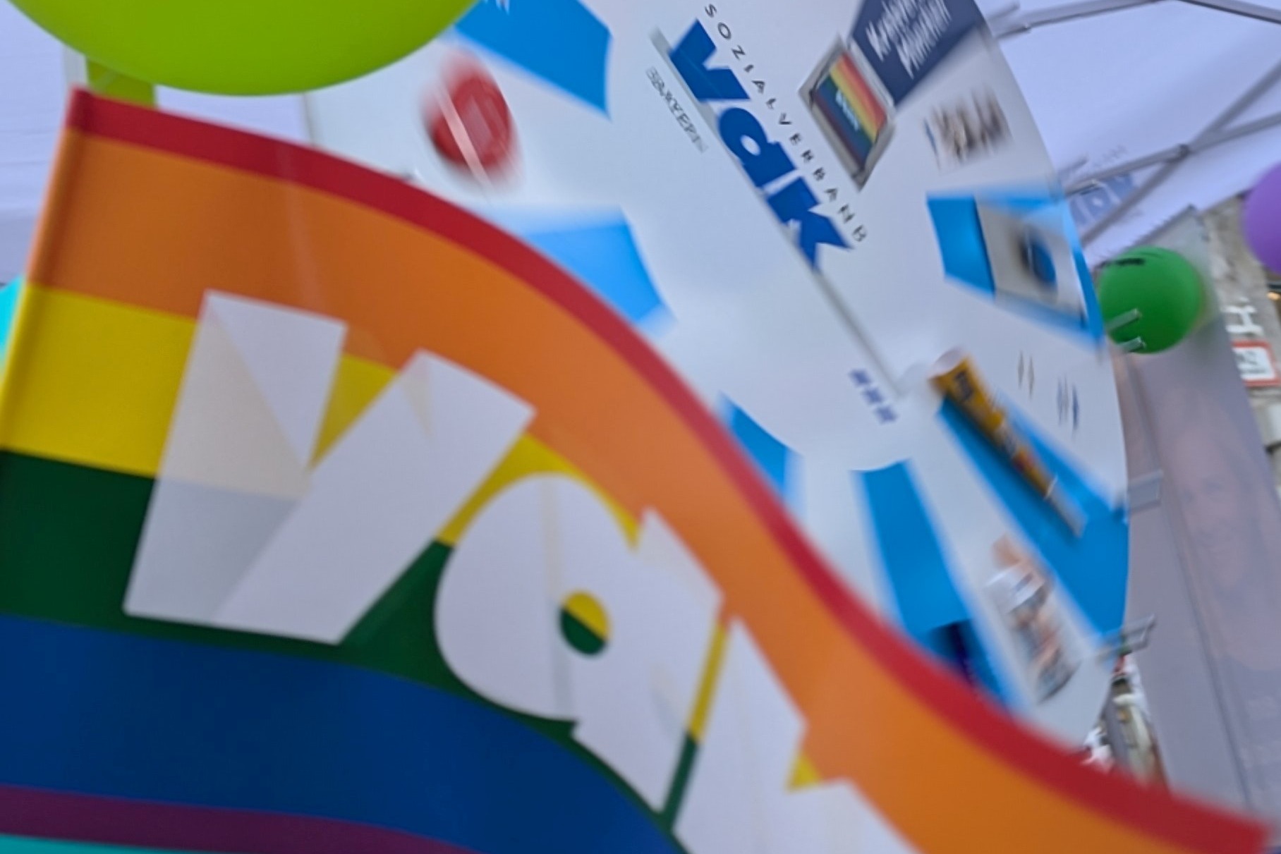 Bild zeigt Regenbogenflagge mit VdK Logo und Gl&uuml;cksrad dahinter