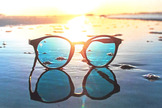 Eine runde Sonnenbrille am Strand mit blauen Gl&auml;sern spiegelt sich in der Abendsonne.